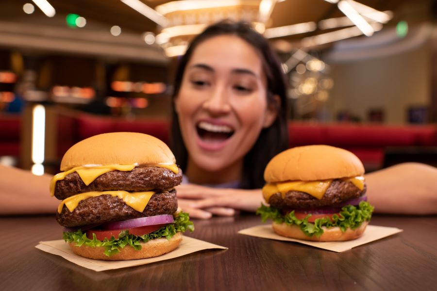 A close up of a woman smiling next to Hard Rock Cafe Sacramento’s ‘The Big Cheeseburger’ and ‘Double-Decker Double Cheeseburger’.