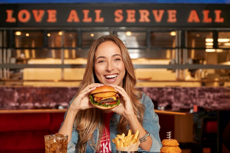 Woman smiles before taking a bite from Hard Rock Cafe’s Original Legendary Burger.
