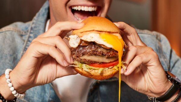 Man smiles as he is about to bite into a mouthwatering burger with a fried egg dripping yolk.