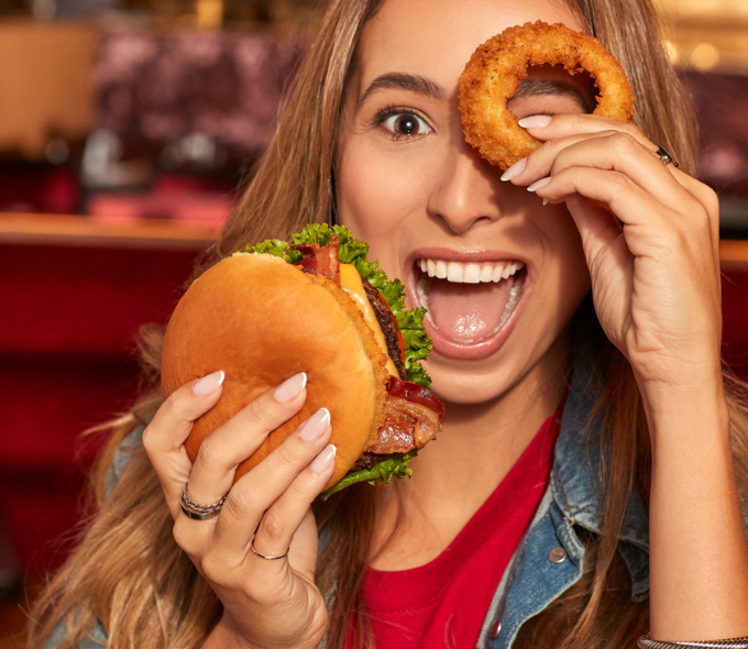 WOMAN HOLDING CHEESEBURGER AND ONION RING SMILING